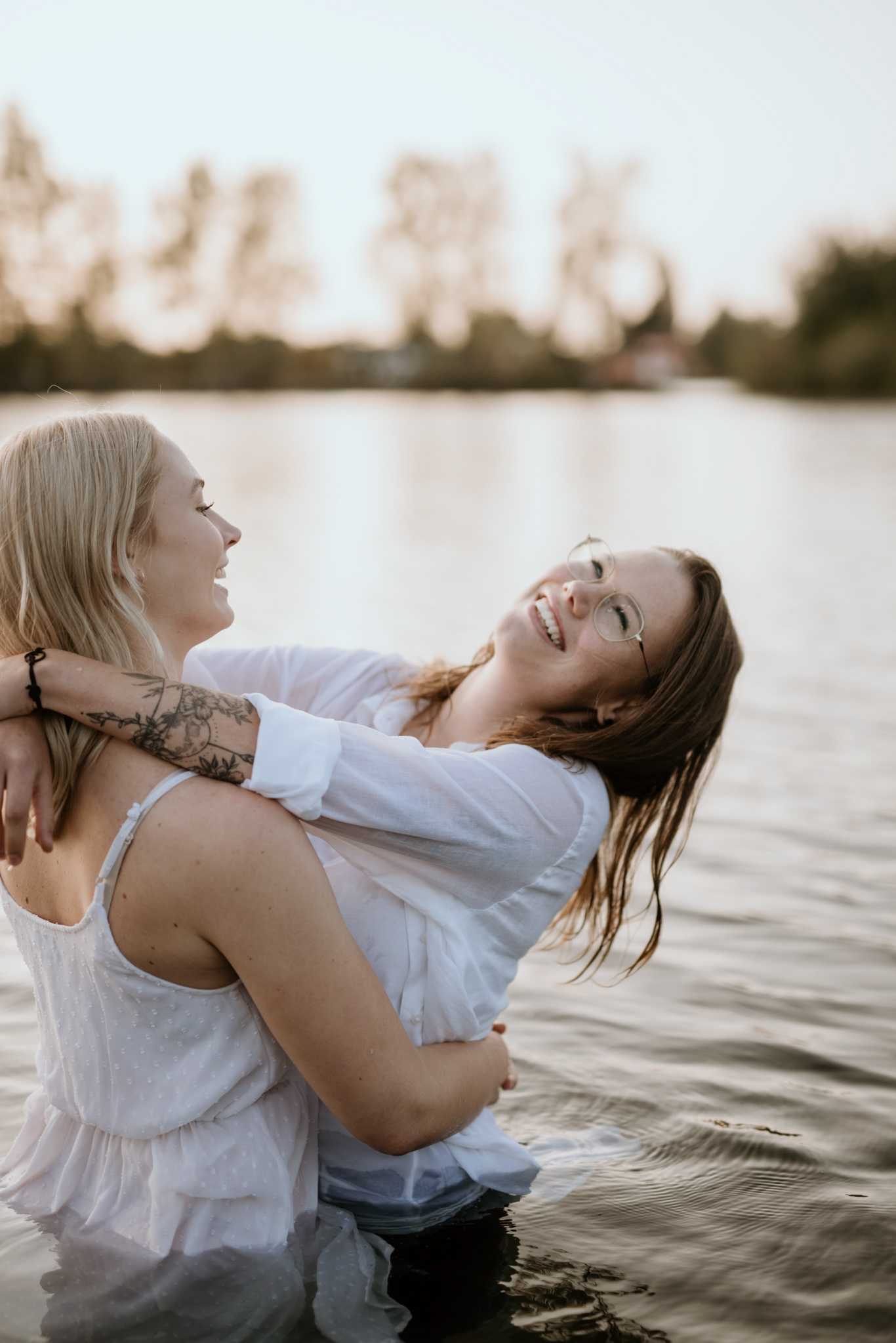 Zwei Frauen lachen ausgelassen im Wasser bei Sonnenuntergang