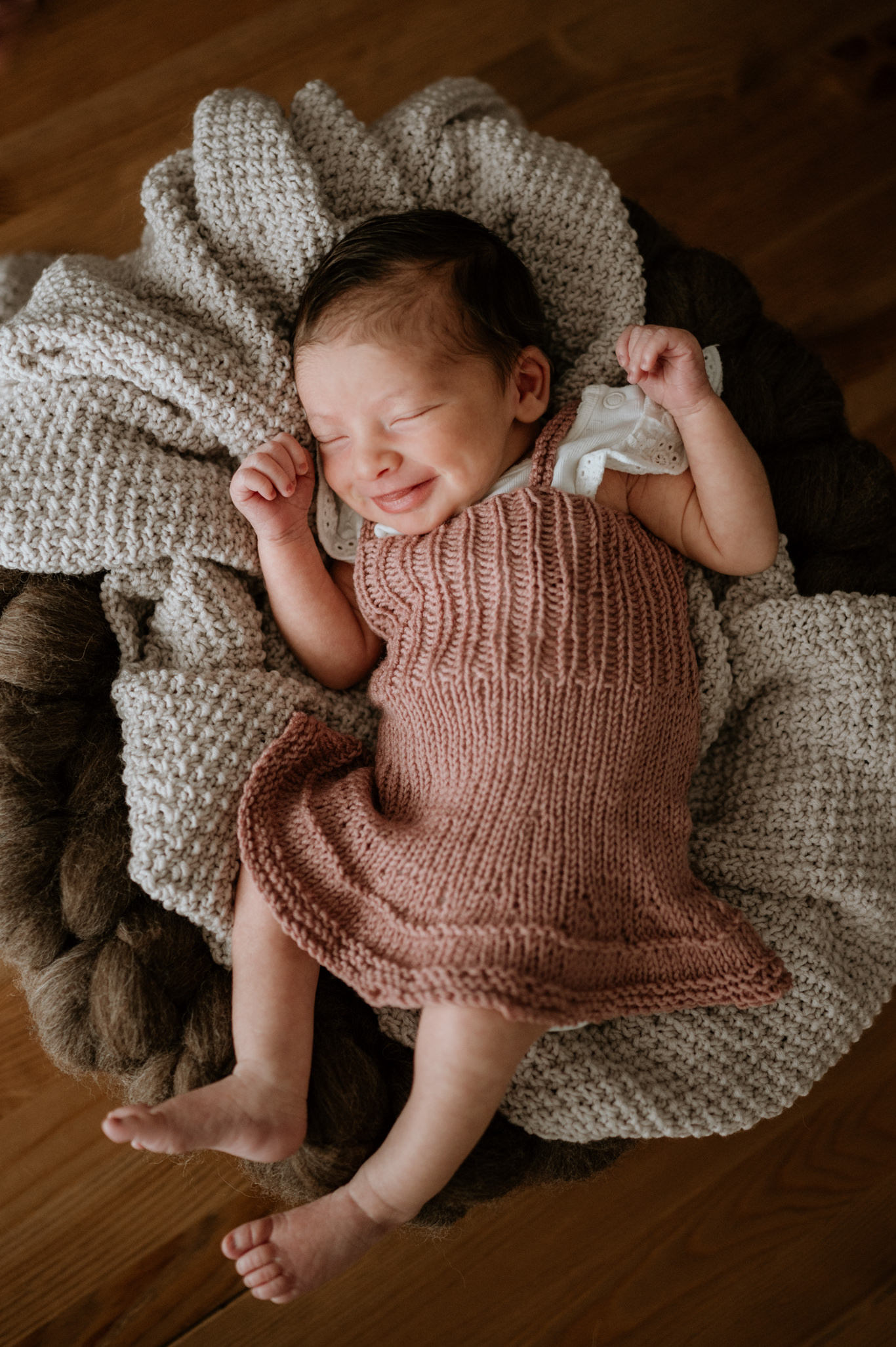 Baby liegt lachend in rosafarbener Strickdecke in einem Korb