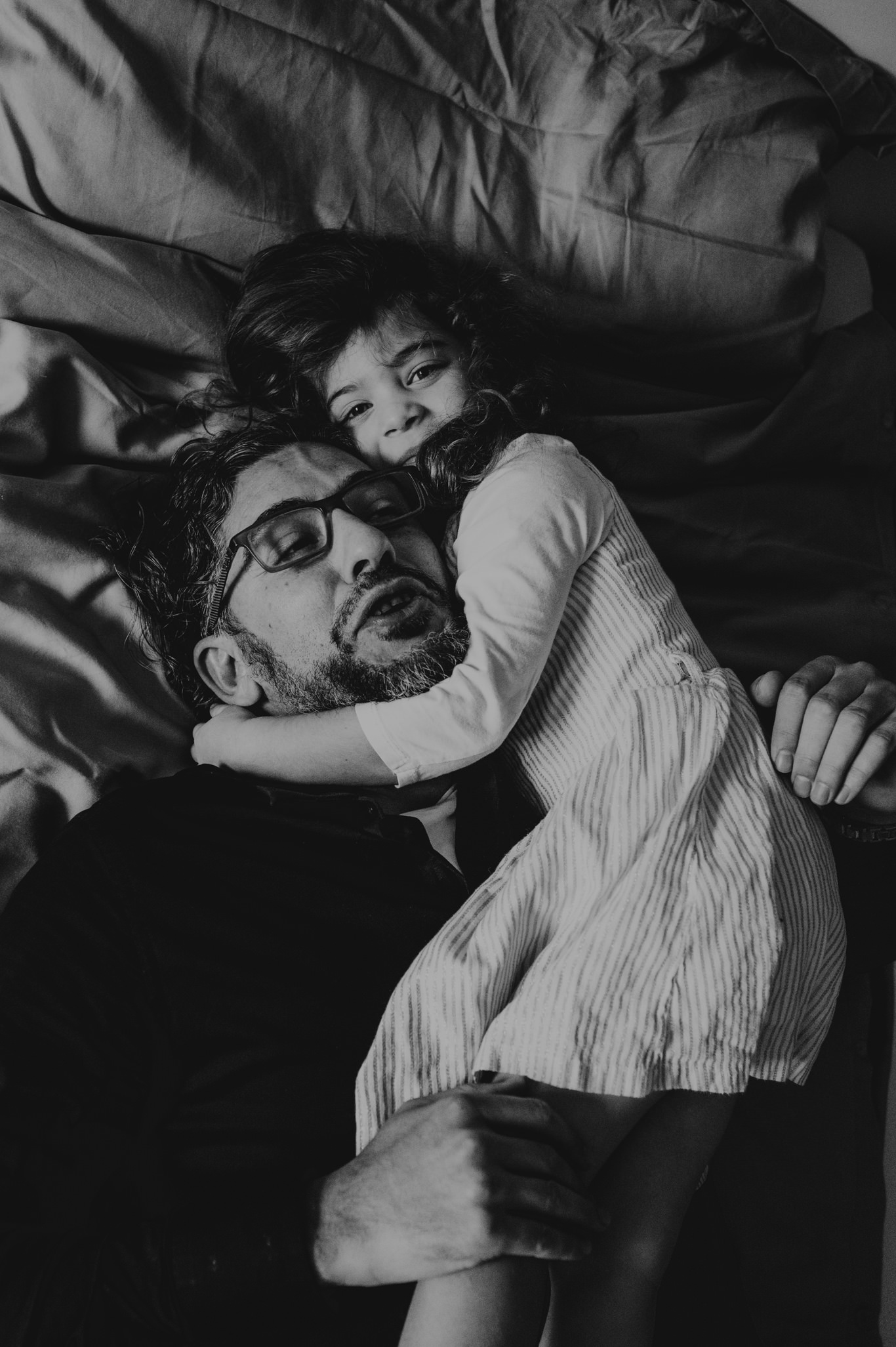 Vater umarmt lachend seine Tochter auf dem Bett, Schwarzweißaufnahme