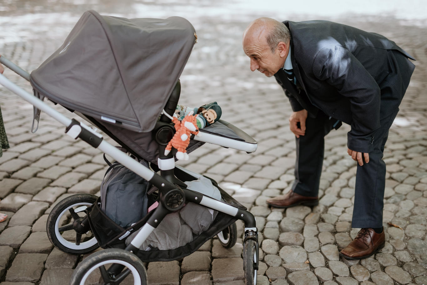 Älterer Mann beugt sich lächelnd über einen Kinderwagen