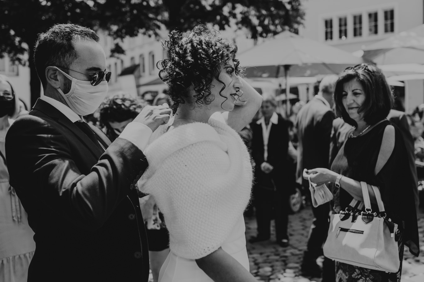 Mann setzt der Braut mit Maske den Schleier auf, Schwarzweißaufnahme