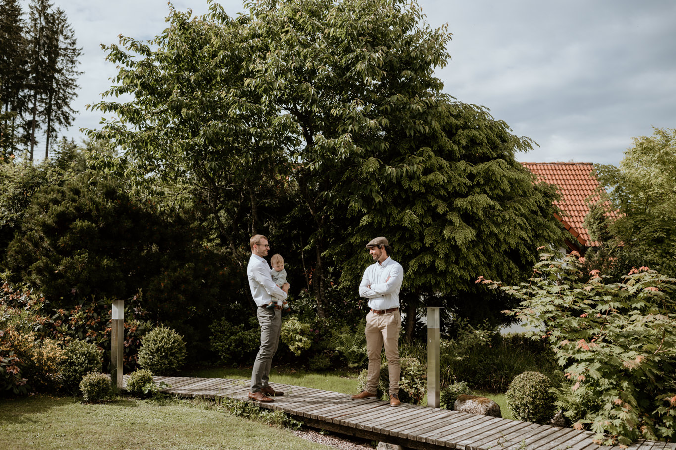 Zwei Trauzeugen warten nebeneinander auf einem Holzsteg im Garten