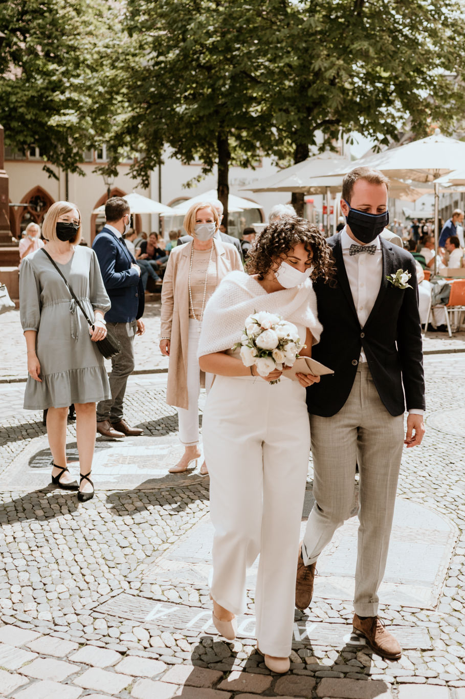 Brautpaar geht mit Maske durch die belebte Fußgängerzone