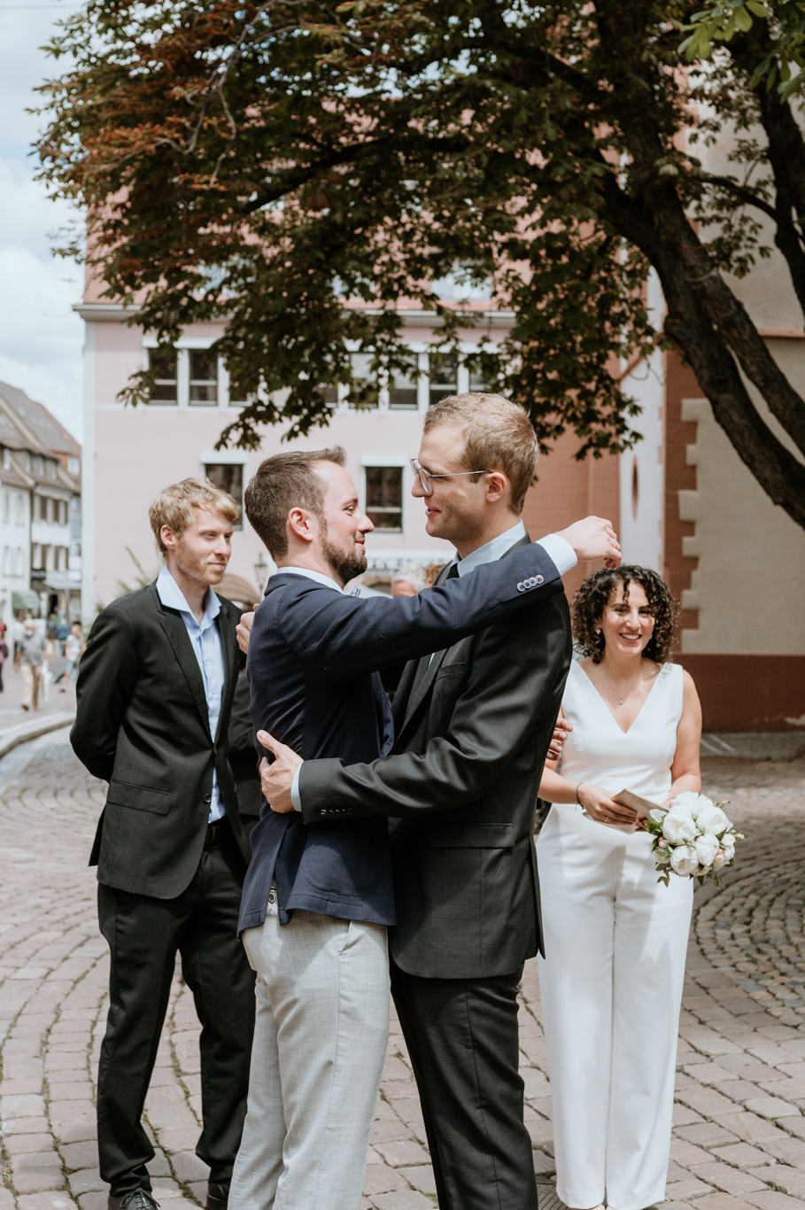Bräutigam wird von zwei Freunden lachend umarmt