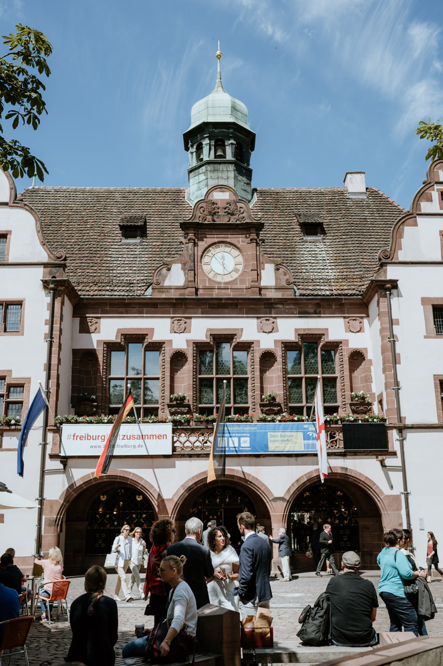 Passanten stehen vor dem historischen Rathaus mit Turm