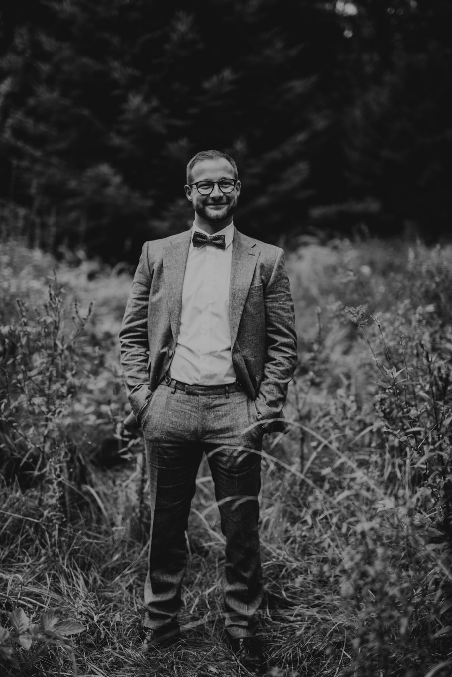 Bräutigam steht mit Händen in den Taschen im Feld, Schwarzweißaufnahme