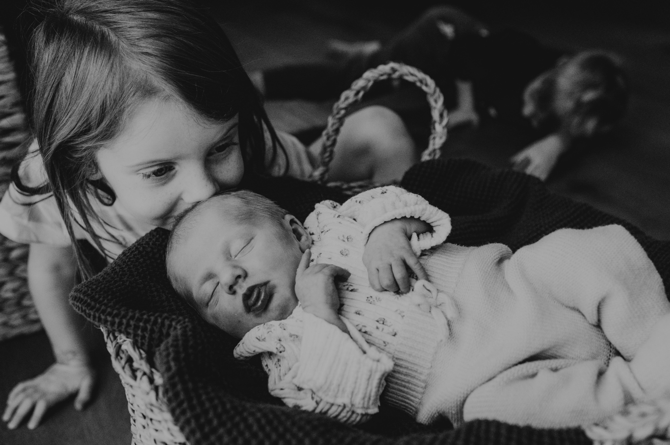 Schwester küsst ihr neugeborenes Geschwisterchen zärtlich, Schwarzweißaufnahme