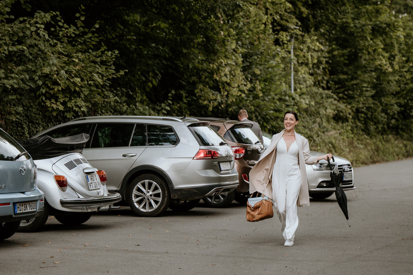 Braut läuft lachend zwischen parkenden Autos über einen Parkplatz