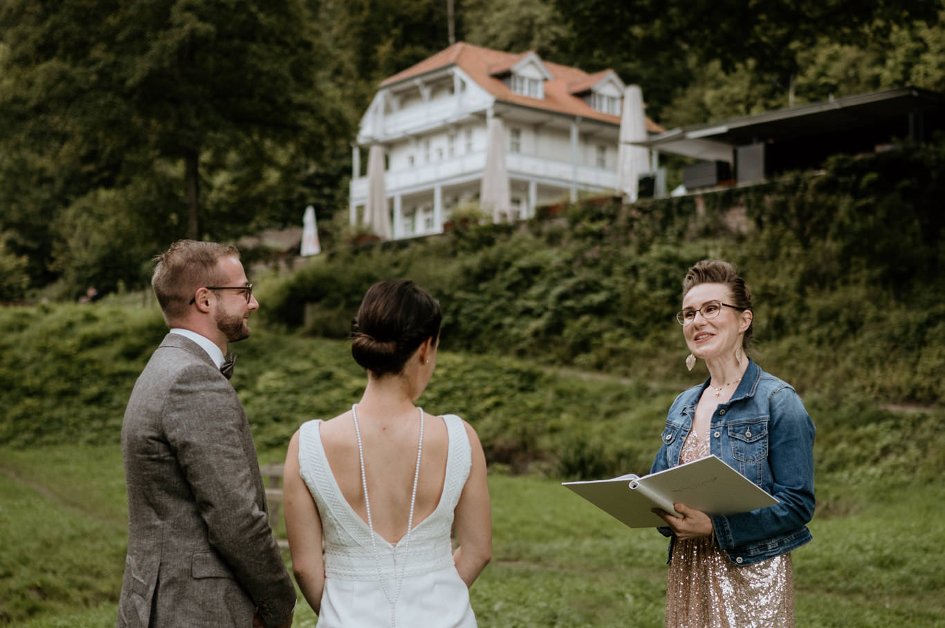 Traurednerin liest vor dem Brautpaar, im Hintergrund eine Villa am Wolfsbrunnen