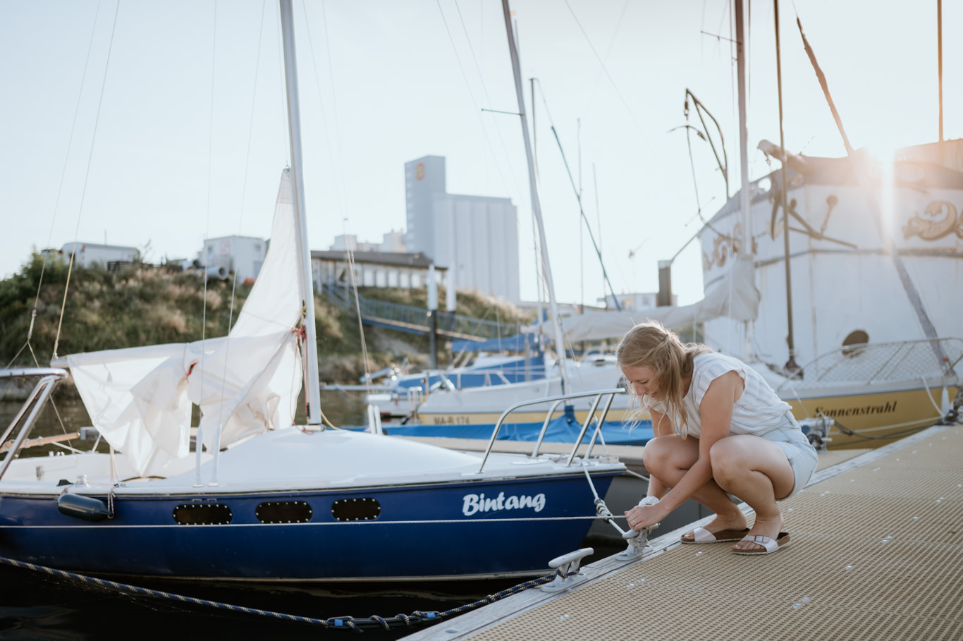 Frau kniet am Segelboot und löst ein Tau am Steg