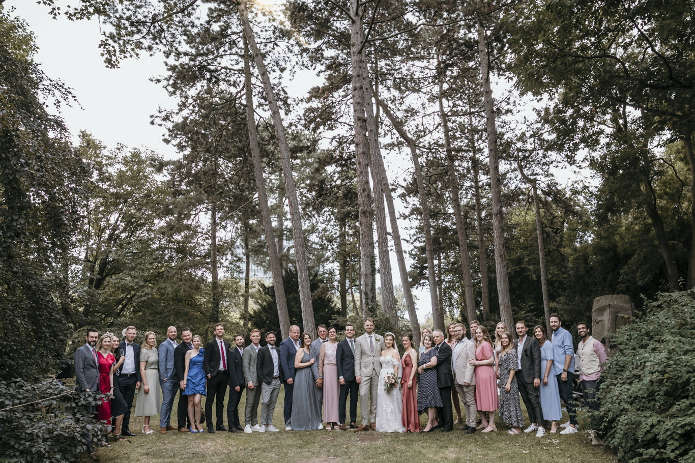Hochzeitsgesellschaft posiert gemeinsam für ein Gruppenfoto zwischen Bäumen
