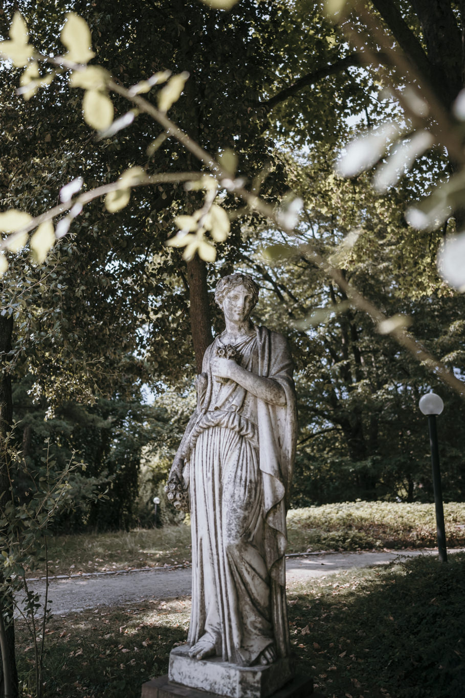 Steinerne Statue steht zwischen Sträuchern im Park