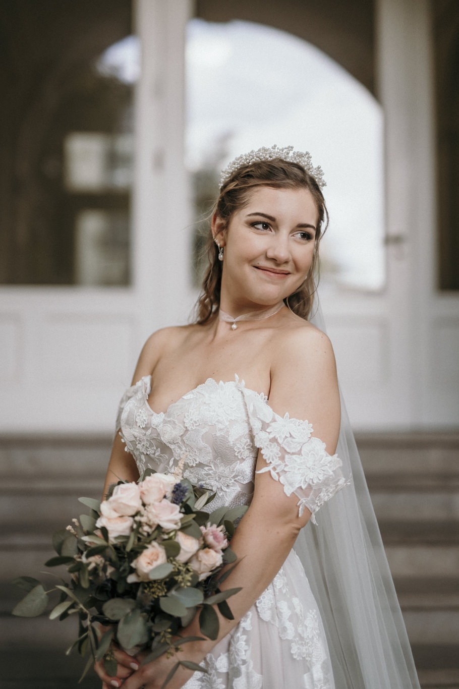 Braut mit Tiara lächelt mit Blumenstrauß in die Kamera