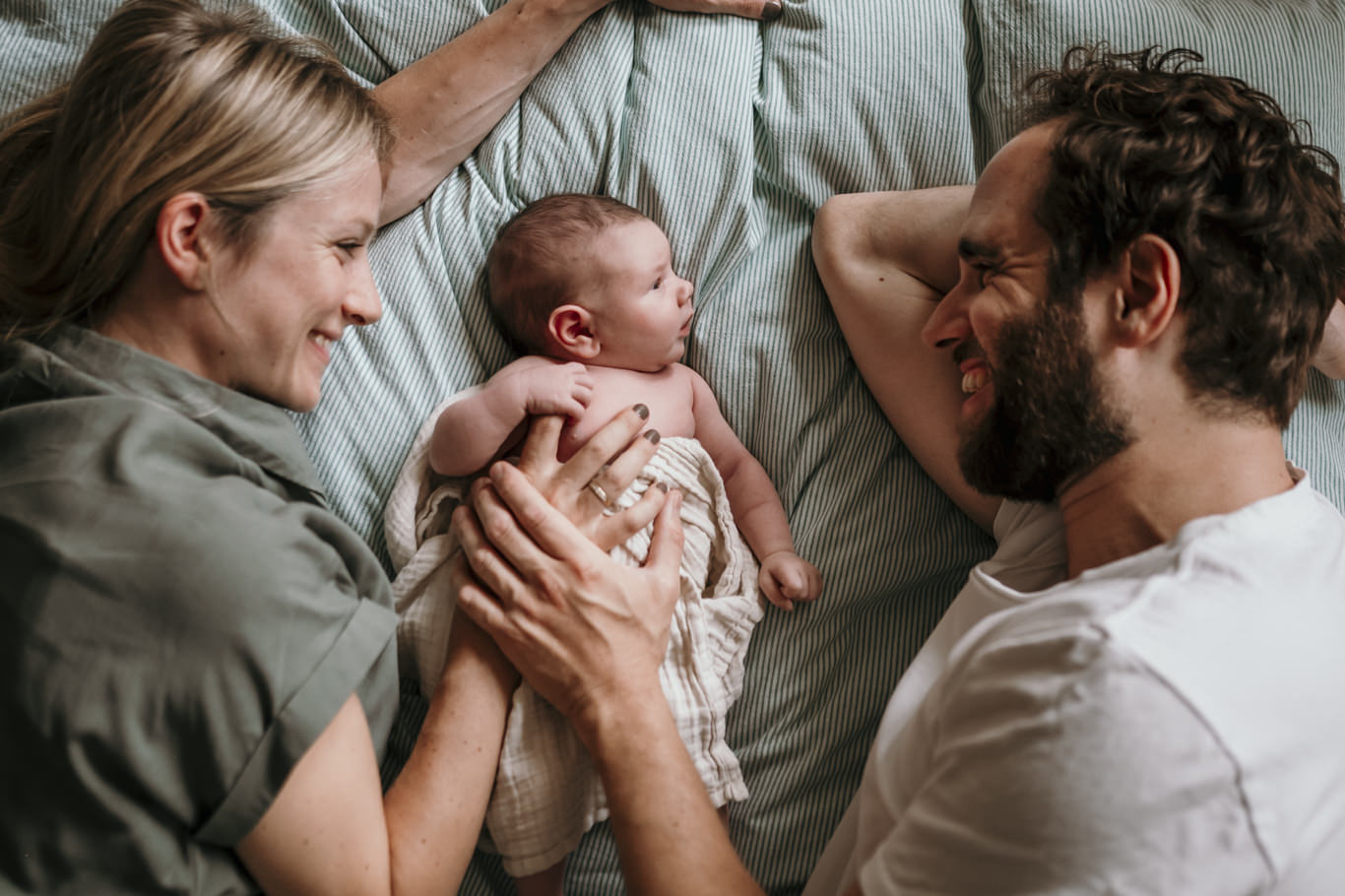 Mutter und Vater liegen lachend mit ihrem Baby zwischen sich