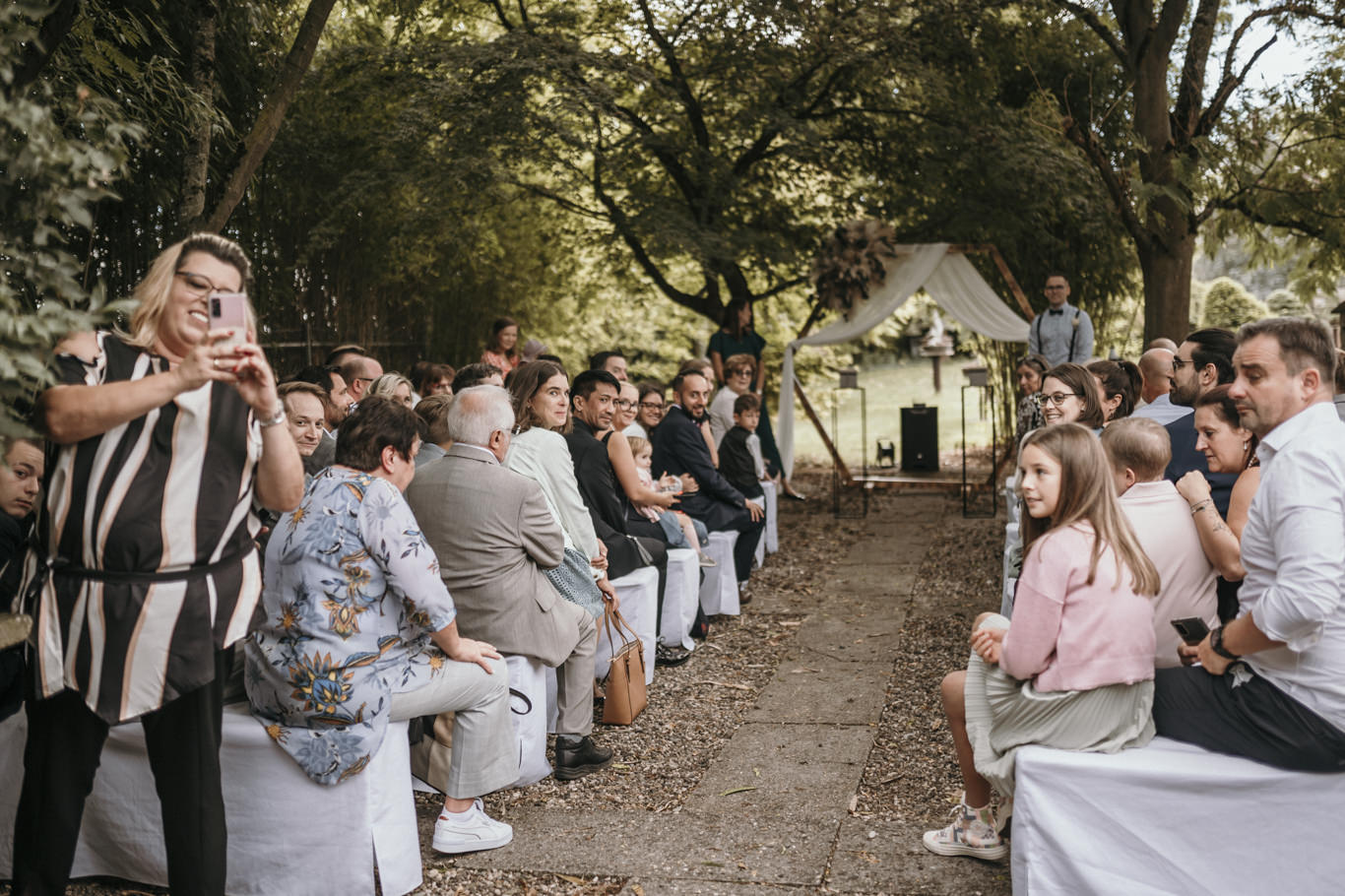 Gäste verfolgen die Trauungszeremonie im Freien und fotografieren mit dem Handy