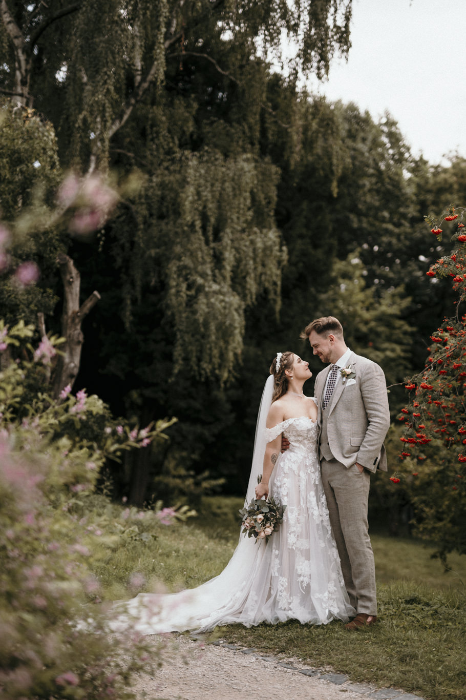 Brautpaar steht umarmt unter einer Trauerweide im Garten