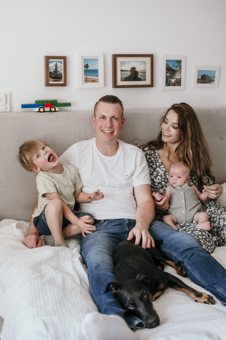 Familie sitzt lachend mit Kleinkind und Baby auf dem Bett