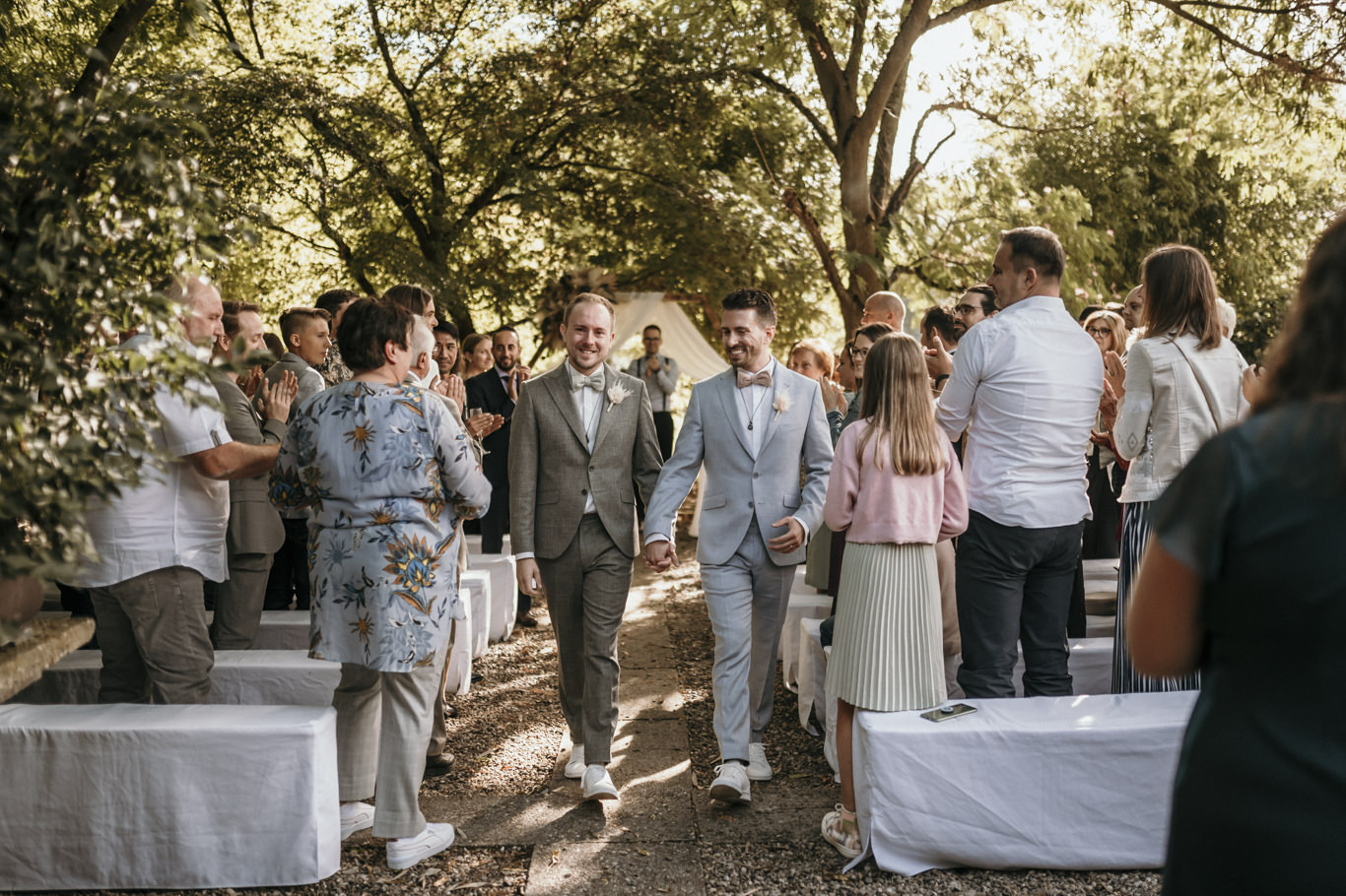 Brautpaar geht Hand in Hand durch die Gästereihen im Garten