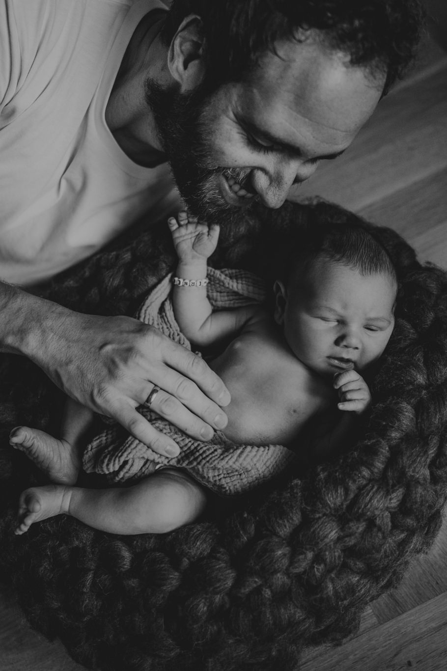 Schwarzweißaufnahme, Vater küsst lachend das Baby auf der Decke