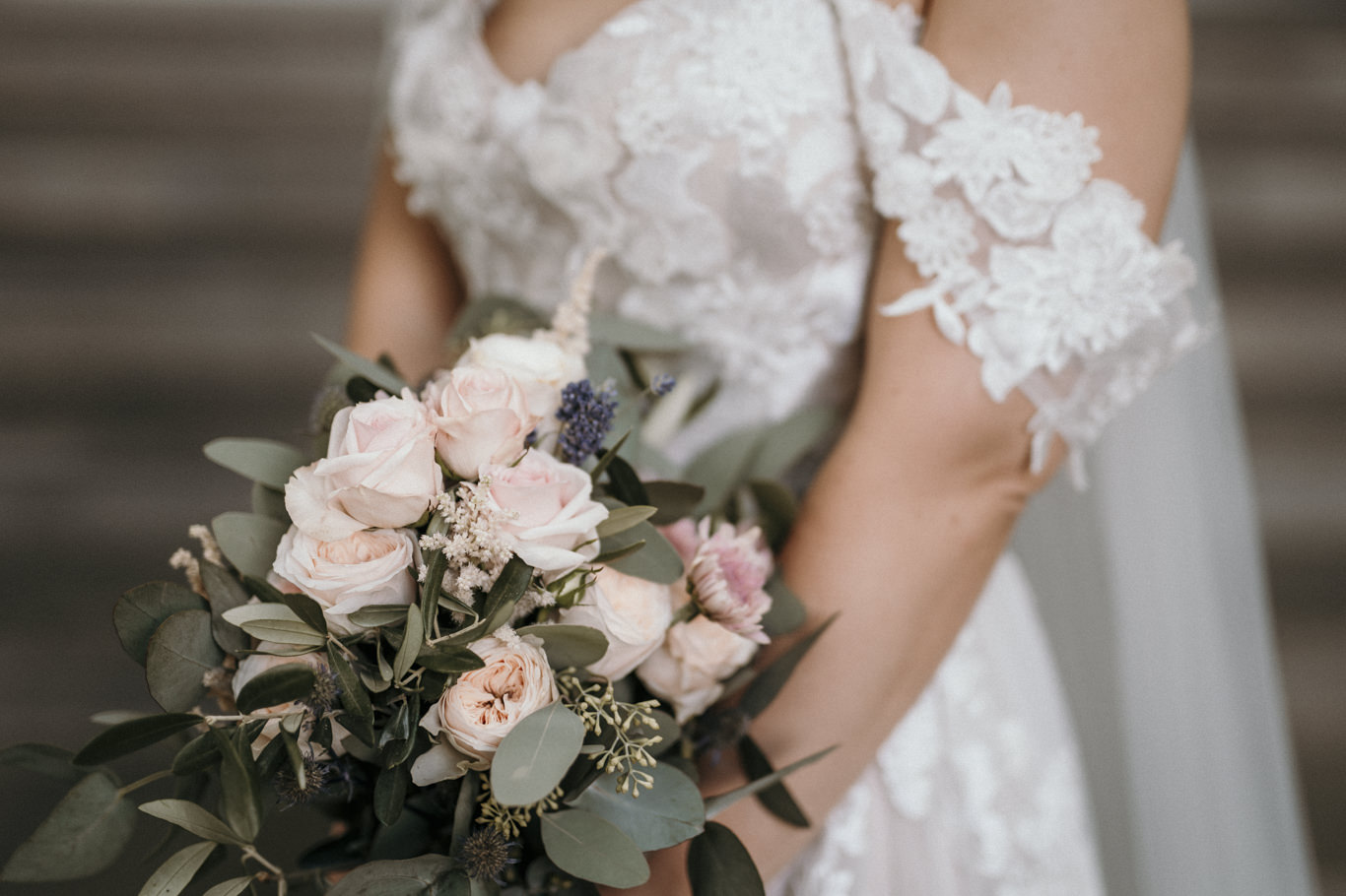 Nahaufnahme von Brautstrauß mit Rosen an Spitzenärmel