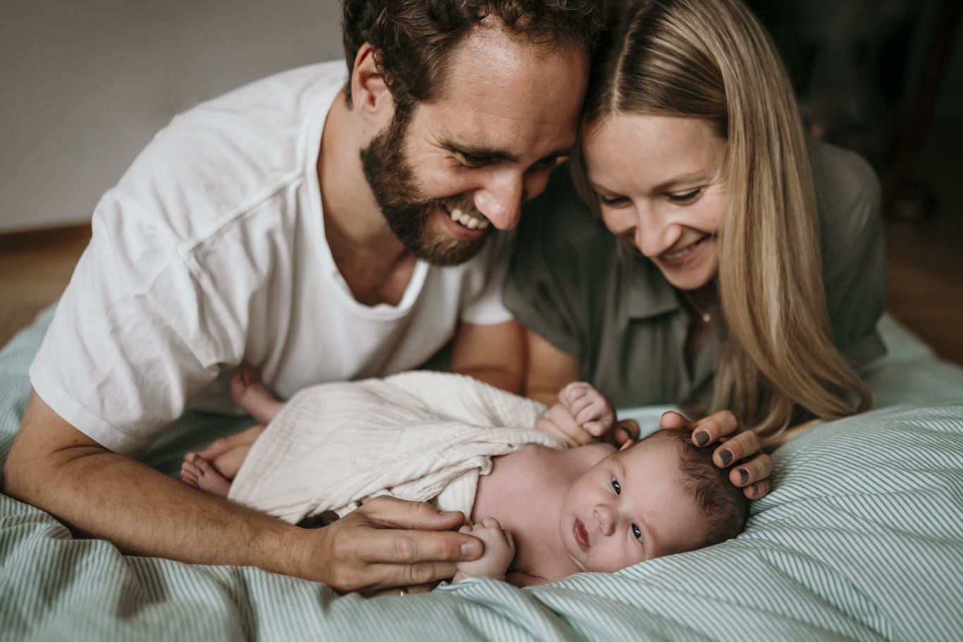 Eltern liegen lächelnd neben ihrem Baby und berühren sein Gesicht
