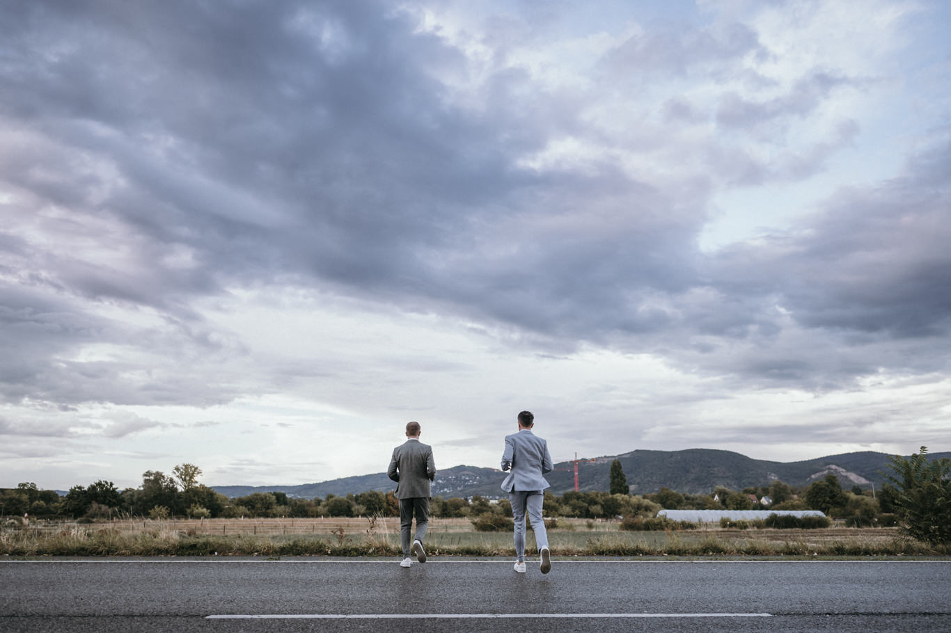 Zwei Bräutigame stehen Hand in Hand unter weiten Wolken