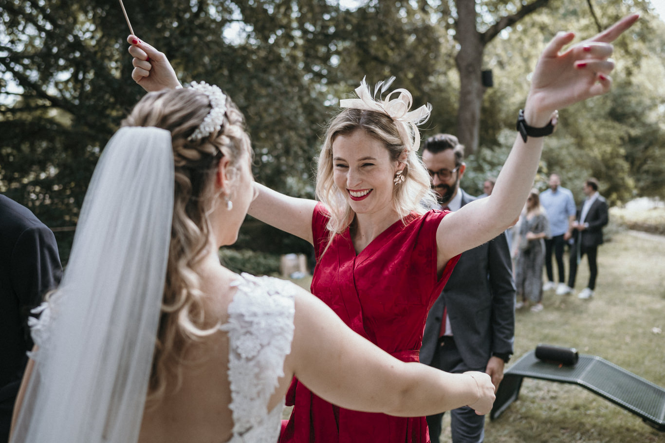 Braut hält lachend die Hände einer Frau im roten Kleid
