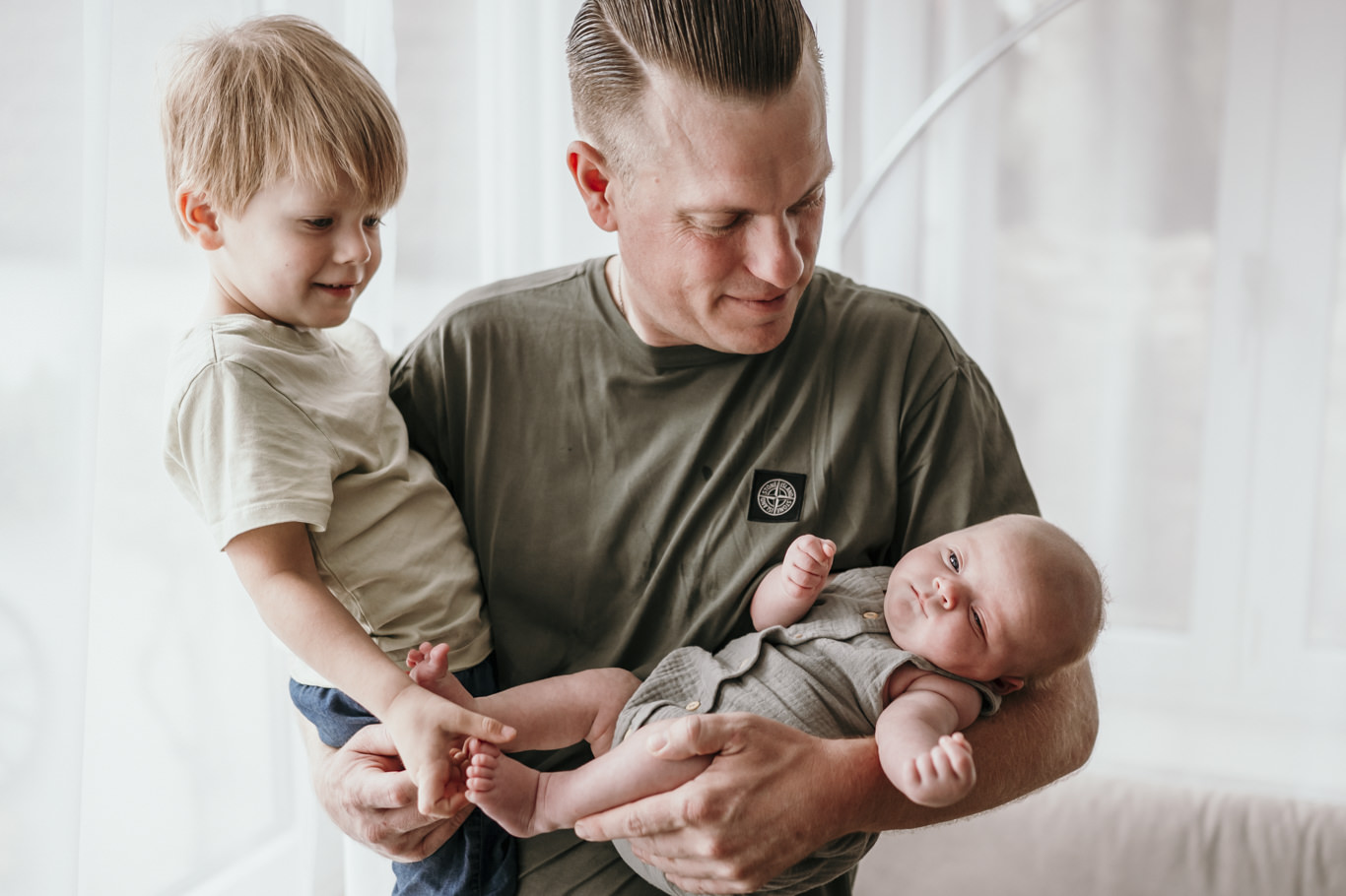 Vater trägt Kleinkind und Neugeborenes gemeinsam auf dem Arm