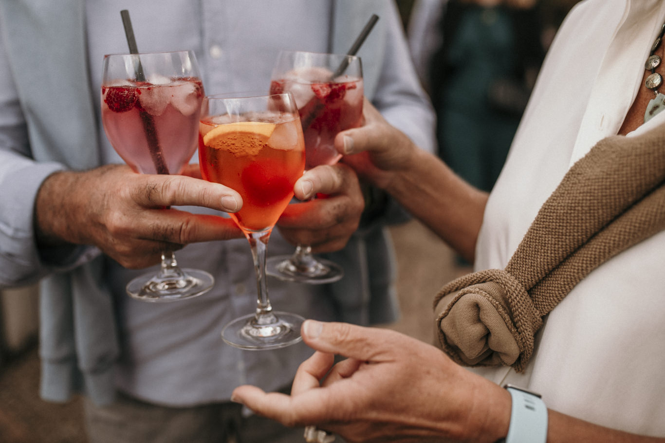 Gäste stoßen lächelnd mit bunten Cocktailgläsern an