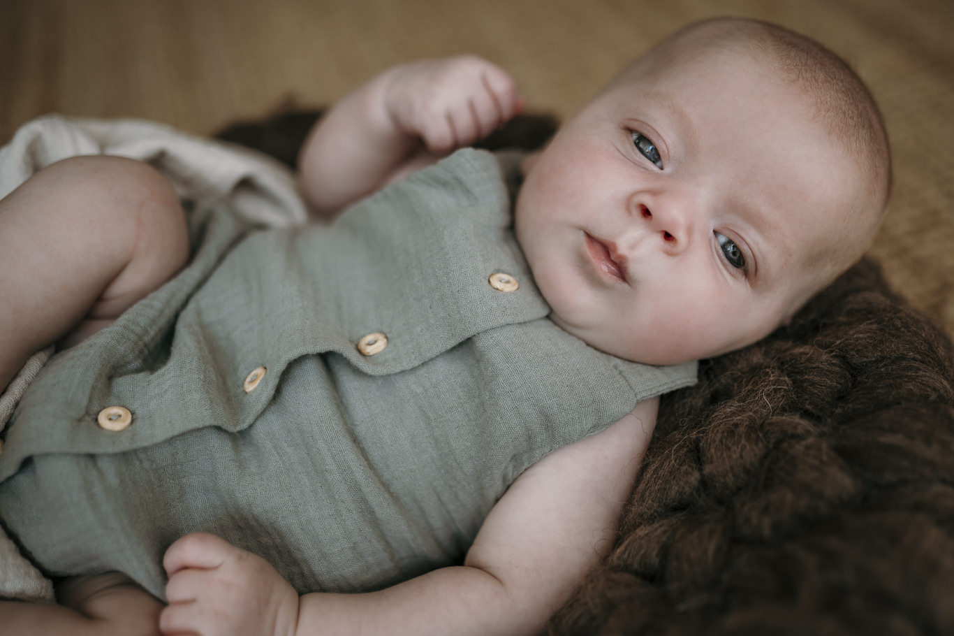 Baby liegt wach in einem Strampler auf einer Wolldecke
