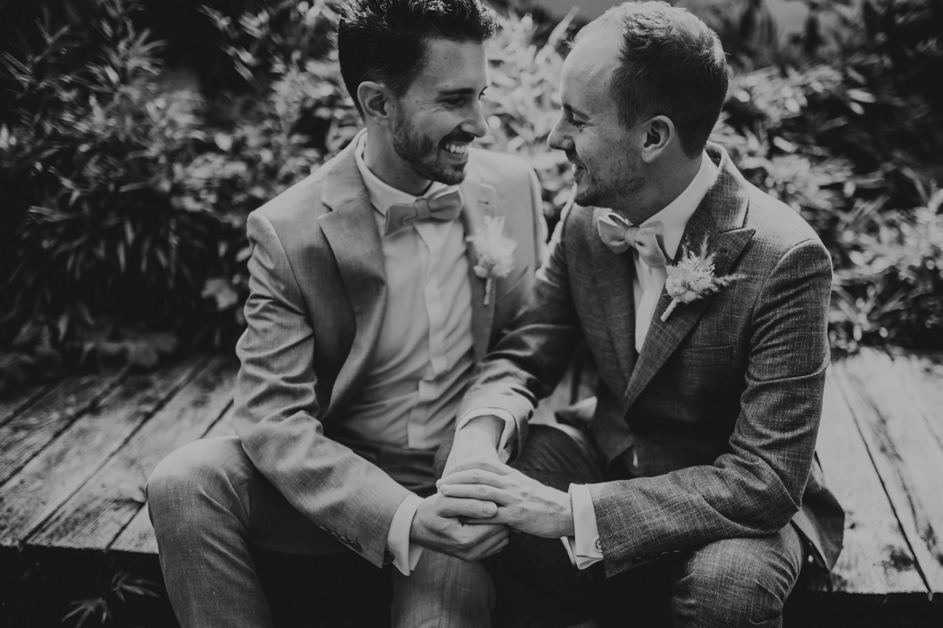 Schwarzweißfoto: Bräutigame sitzen Hand in Hand und lachen sich an