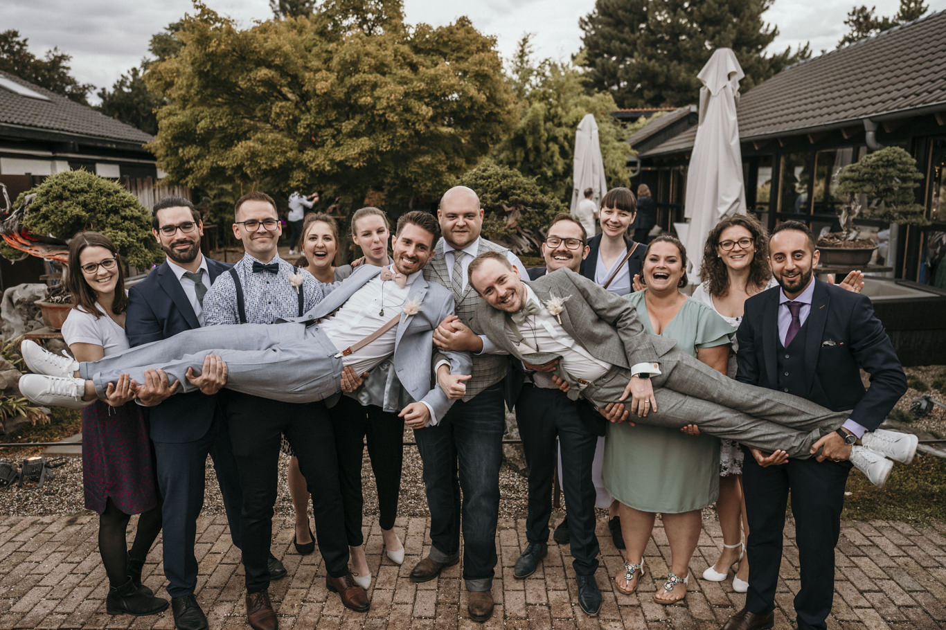 Freunde tragen lachend einen Gast auf Händen im Garten