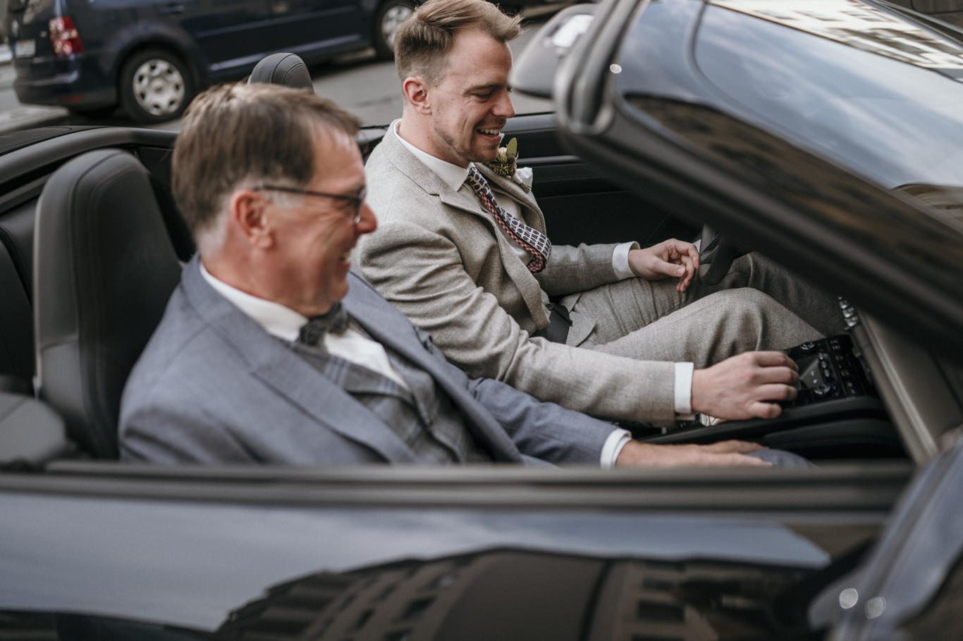 Zwei Männer sitzen lächelnd im offenen Cabriolet