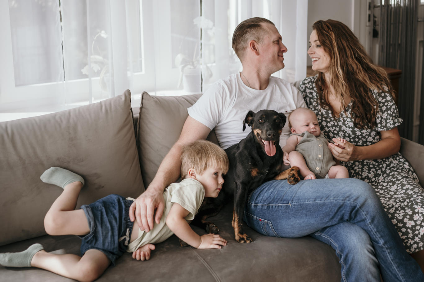 Familie mit zwei Kindern und Hund kuschelt gemeinsam auf dem Sofa