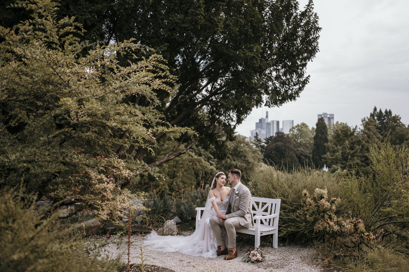 Brautpaar sitzt Hand in Hand auf einer Bank im herbstlichen Garten im Palmengarten Frankfurt bei einer Hochzeit