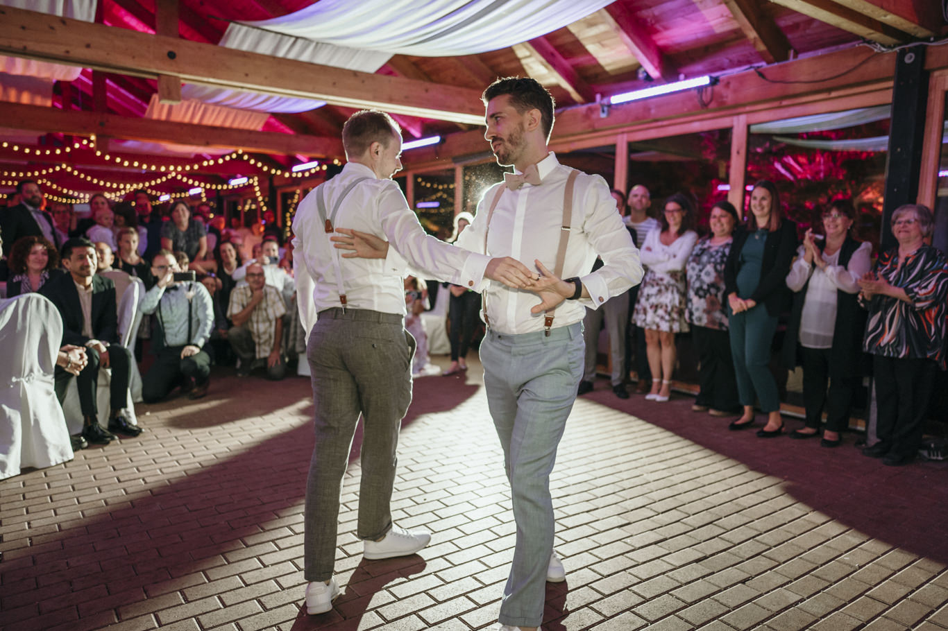 Zwei Bräutigame tanzen ausgelassen unter bunten Partylichtern