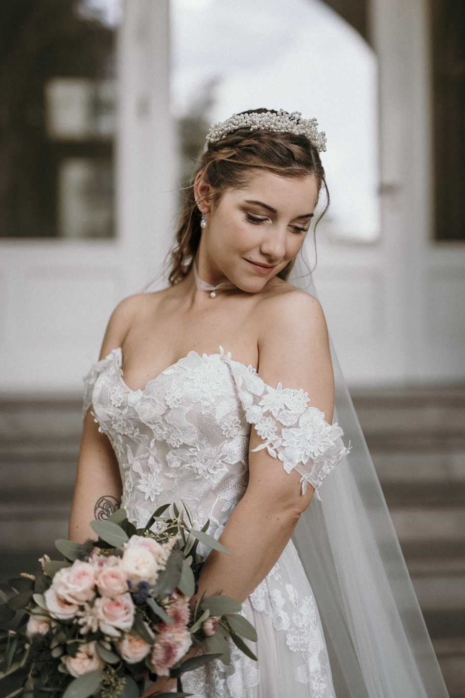Braut mit Tiara blickt lächelnd auf ihren Blumenstrauß