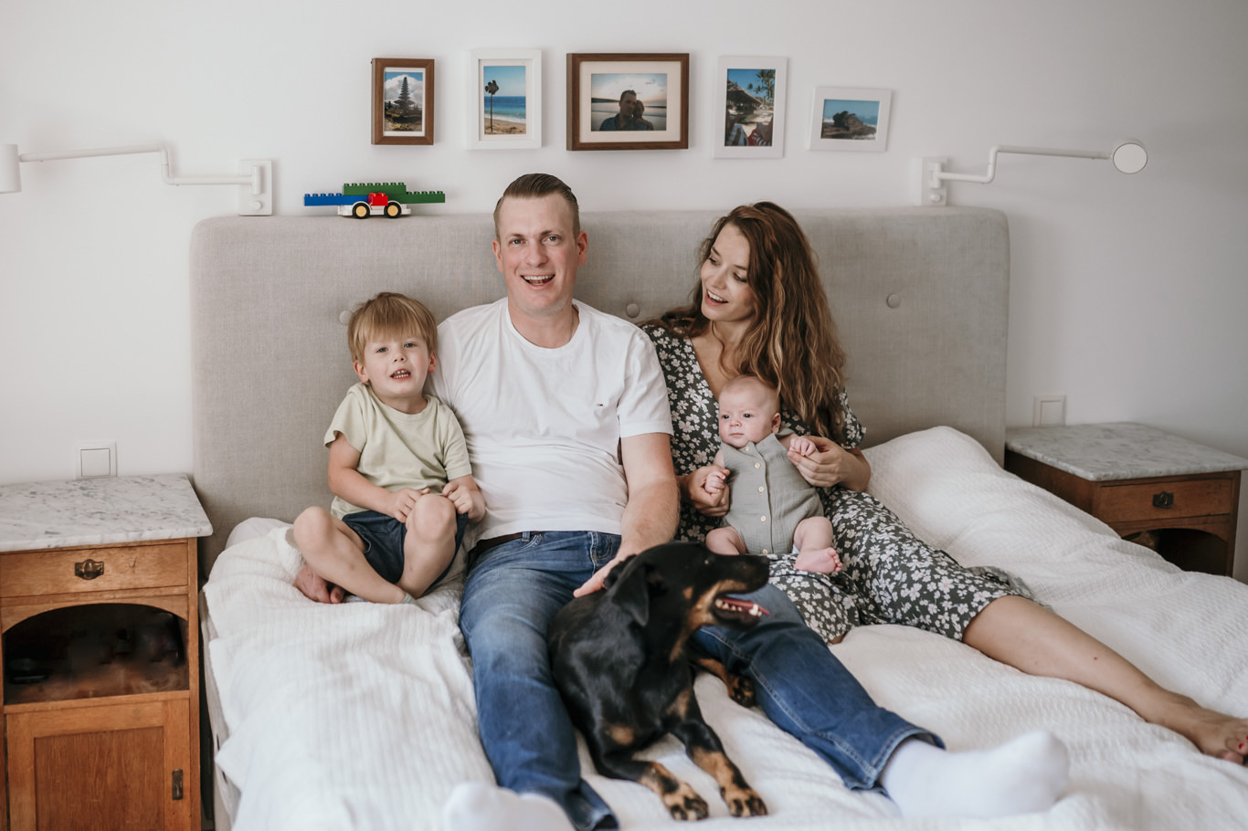 Eltern sitzen mit zwei Kindern und Hund auf dem Bett