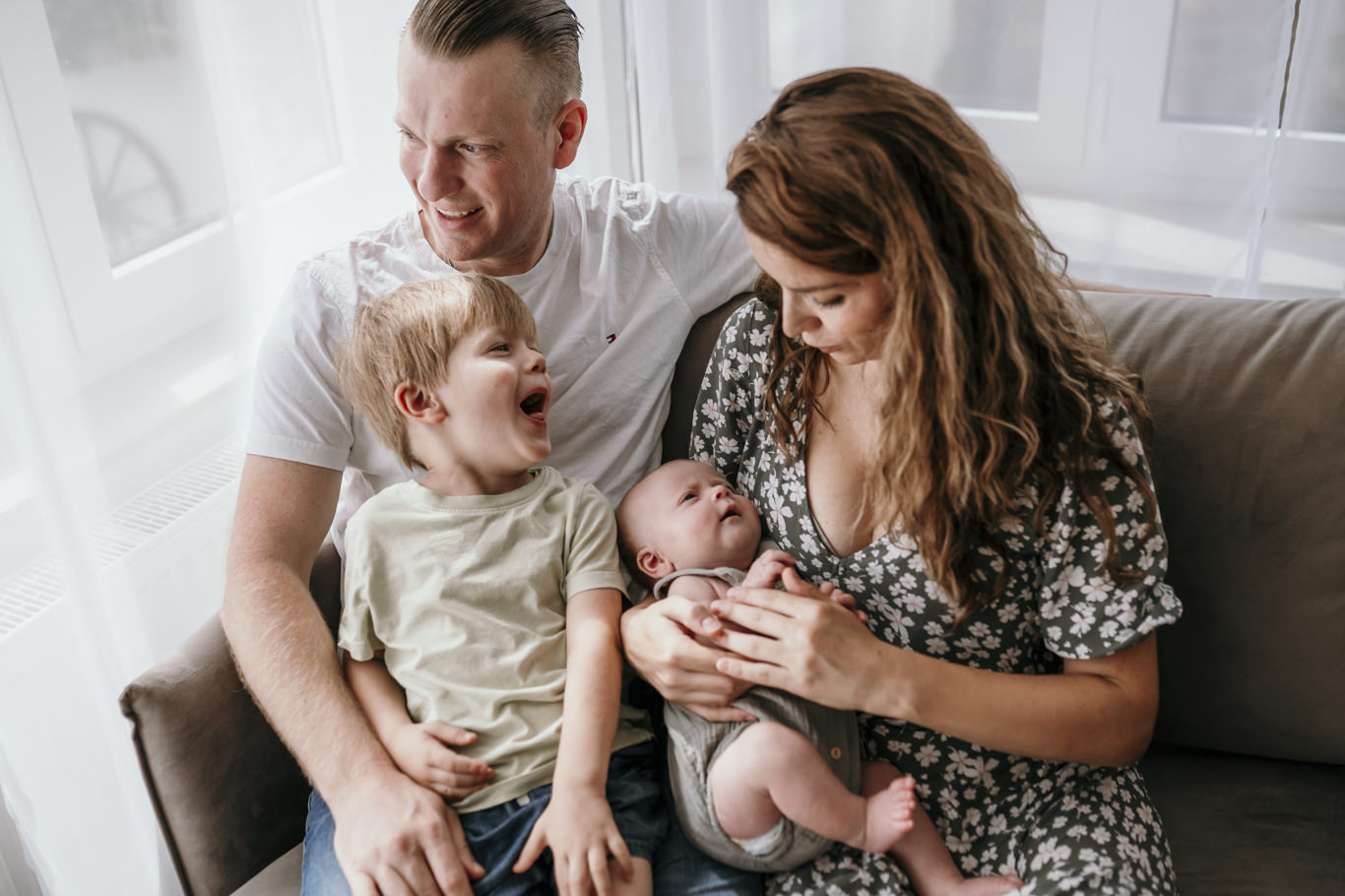 Eltern lachen ausgelassen mit Kleinkind und Baby auf dem Sofa