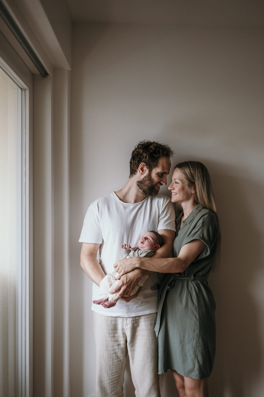 Eltern stehen lächelnd am Fenster mit ihrem Baby im Arm
