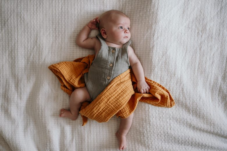 Baby liegt strampelnd auf dem Bett unter einer orangefarbenen Decke