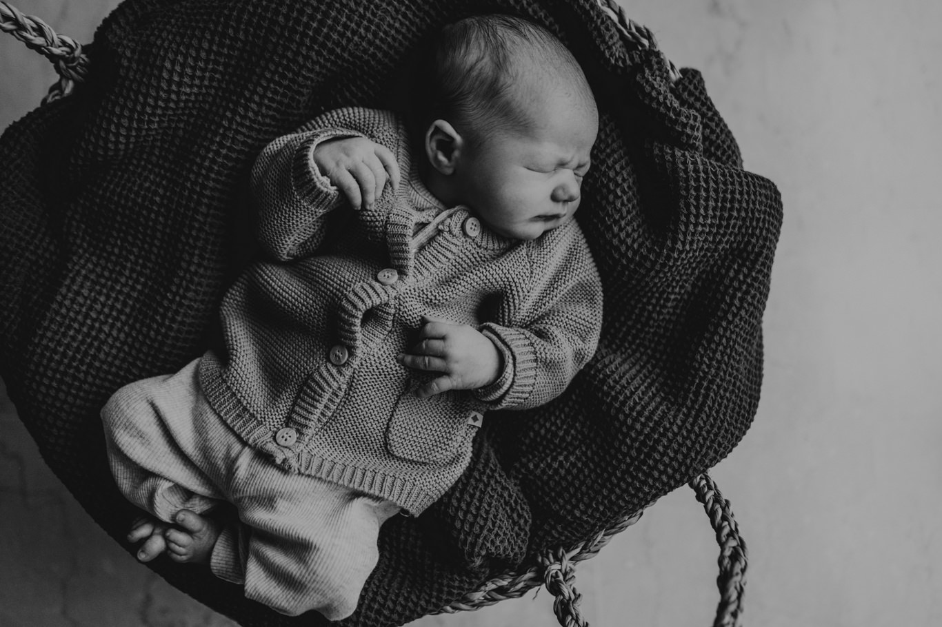 Schwarzweißaufnahme eines schlafenden Babys in Wolltuch gebettet
