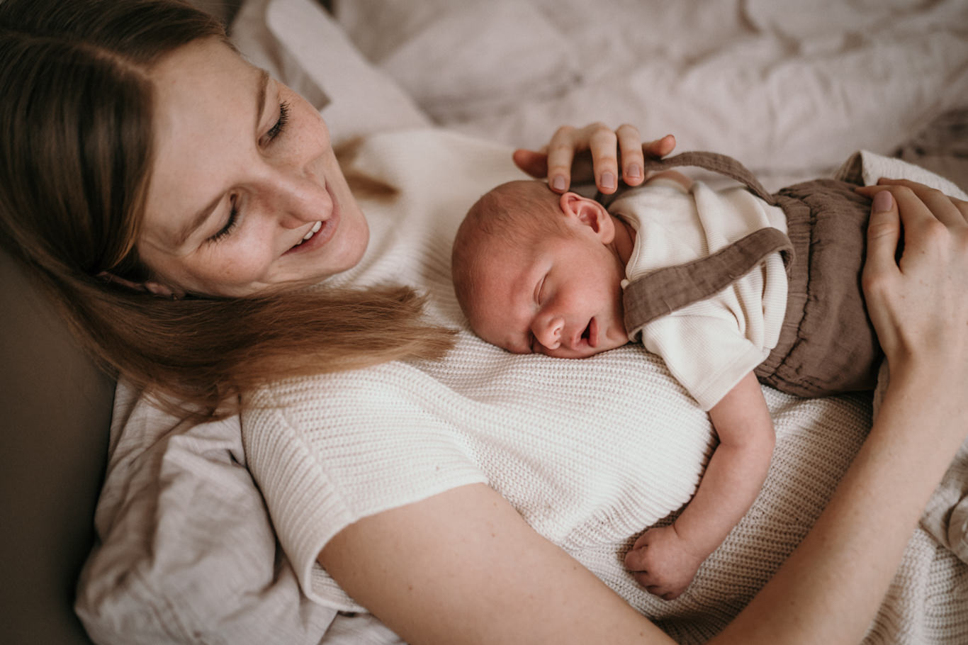 Mutter hält lächelnd ihr schlafendes Baby im Bett