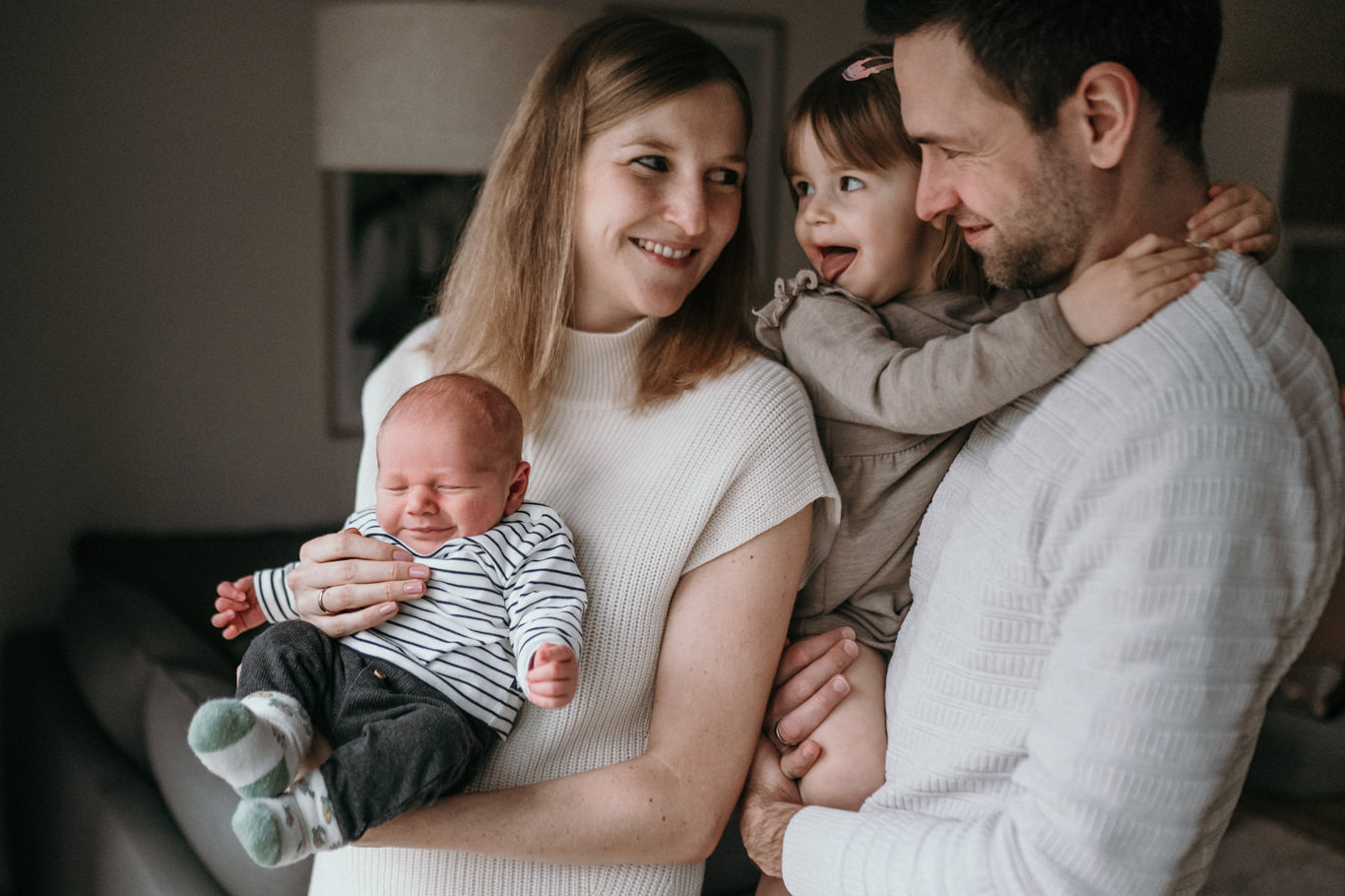 Eltern sitzen lächelnd mit Baby und Kind auf dem Sofa