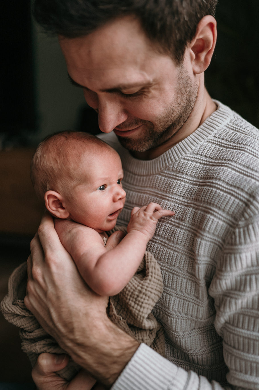 Vater hält lächelnd sein Baby im Arm und blickt es an
