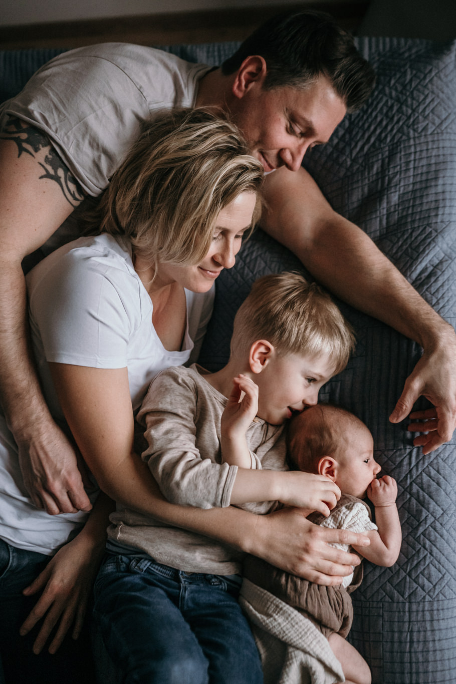 Familie liegt kuschelnd auf dem Bett mit ihrem Neugeborenen