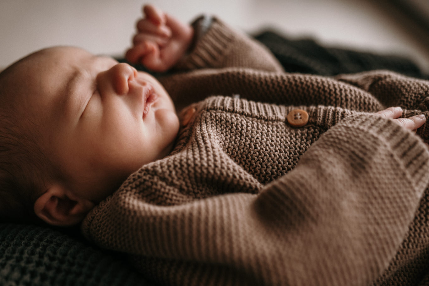 Schlafendes Baby liegt eingewickelt in eine braune Wolldecke