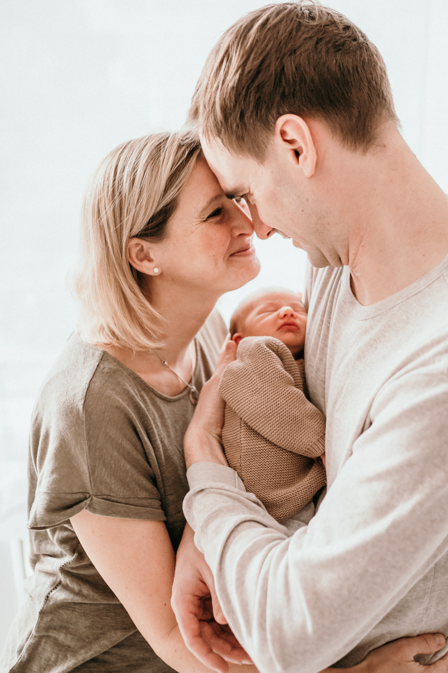 Eltern halten ihr Baby zwischen sich und lächeln sich an