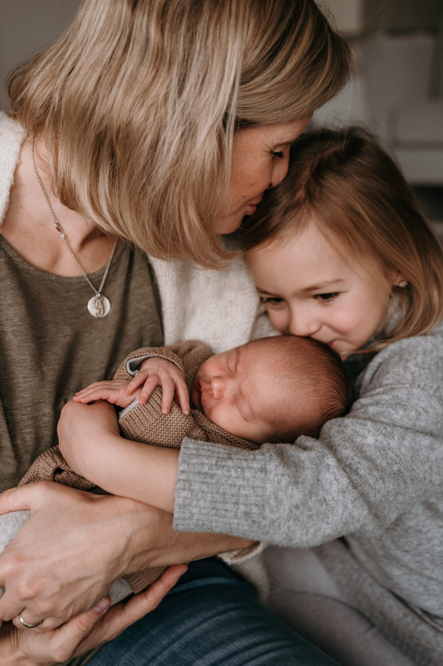 Mutter und Kind küssen gemeinsam das Baby auf der Wange