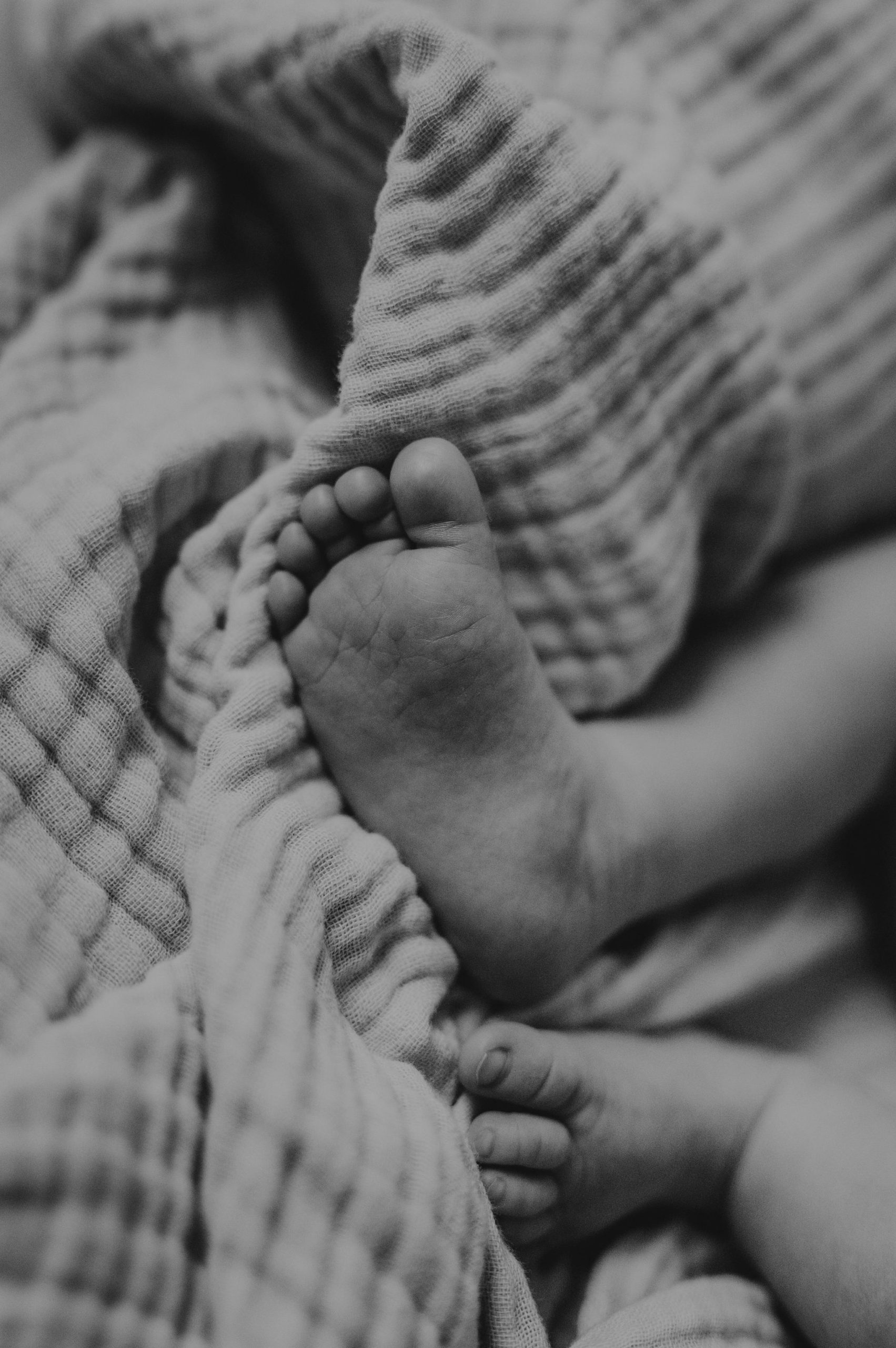 Schwarzweißaufnahme winziger Babyfüße in einer gestreiften Decke